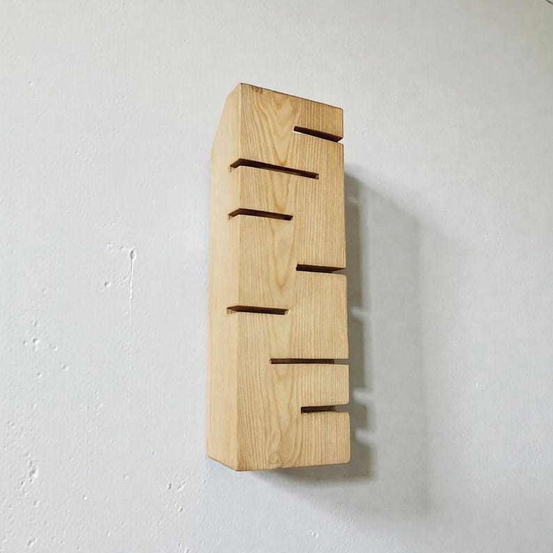 A vertical rectangular wooden wall sconce with warm LED light shining through carved horizontal openings. The wood has a natural grain and rustic brown finish. The style is minimalist, cozy, and modern, suitable for hallway, living room, or bedroom wall lighting.