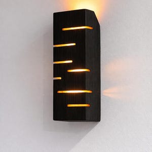 A vertical rectangular wooden wall sconce with warm LED light shining through carved horizontal openings. The wood has a natural grain and rustic brown finish. The style is minimalist, cozy, and modern, suitable for hallway, living room, or bedroom wall lighting.