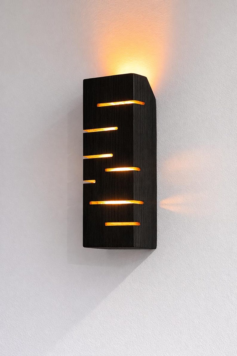 A vertical rectangular wooden wall sconce with warm LED light shining through carved horizontal openings. The wood has a natural grain and rustic brown finish. The style is minimalist, cozy, and modern, suitable for hallway, living room, or bedroom wall lighting.
