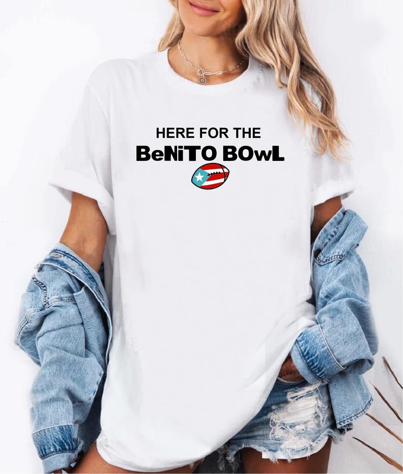 May include: White t-shirt with the text "HERE FOR THE BeNiTO BOWL" in black, with a football graphic featuring the Puerto Rican flag. The shirt is worn with a denim jacket.