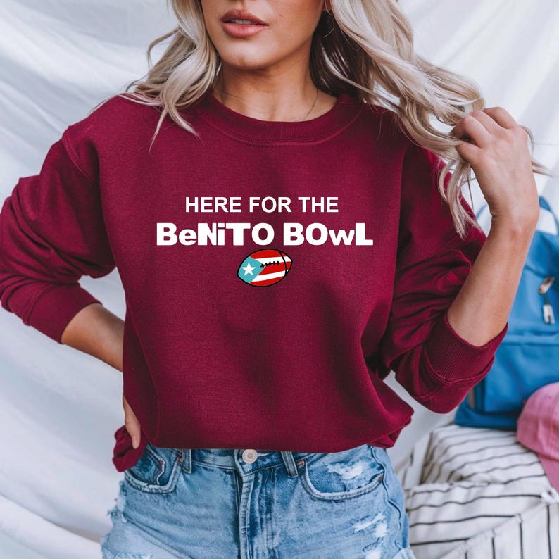 May include: A maroon sweatshirt with the text "HERE FOR THE BeNITO BOWL" in white. The word "BOWL" features a football graphic with the Puerto Rican flag. The sweatshirt is a casual garment.