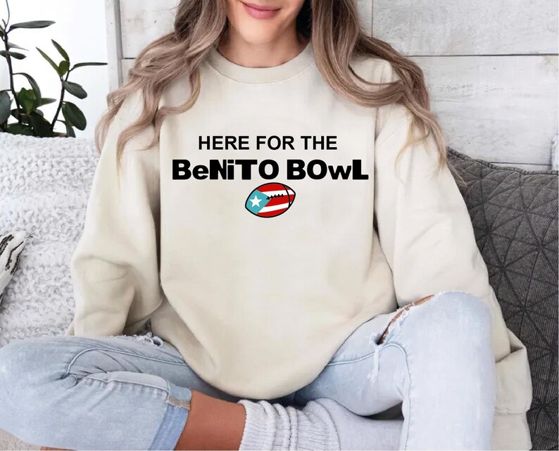 May include: Cream-colored sweatshirt with the text "HERE FOR THE BeNiTO BOWL" in black. A football graphic with the Puerto Rican flag is below the text. The sweatshirt is worn by a person.
