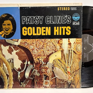 May include: Vintage vinyl record album cover for Patsy Cline's Golden Hits. The cover features a portrait of Patsy Cline, with the album title in large gold letters. The background includes western-themed imagery, including a saddle and spurs.