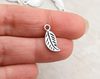 May include: Silver-colored leaf charms with a loop at the top for jewelry making. The charms have detailed veining and a slightly textured surface. Several charms are visible, with one held in a hand.