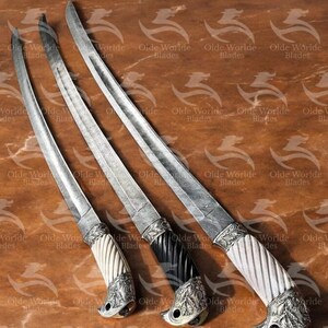 May include: Three decorative swords with intricate metalwork and ornate handles. The handles are made of wood and have a twisted design. The swords are on a wooden surface.
