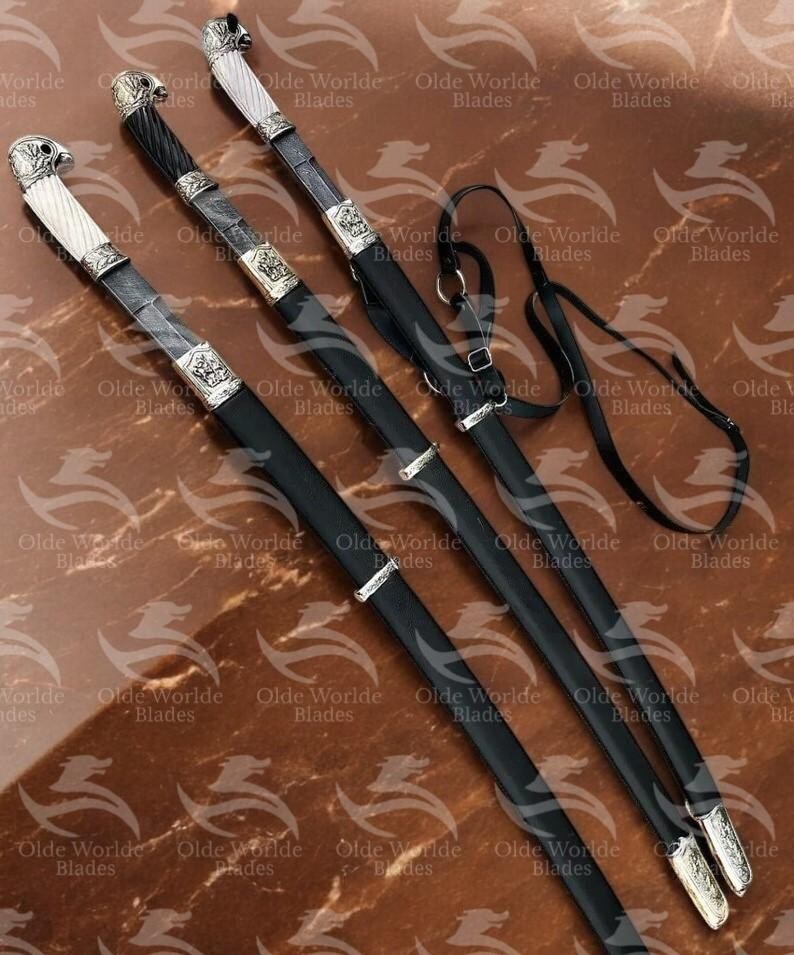 May include: Three black leather-wrapped swords with silver accents and ornate handles. The swords are displayed on a brown surface with a black leather strap.