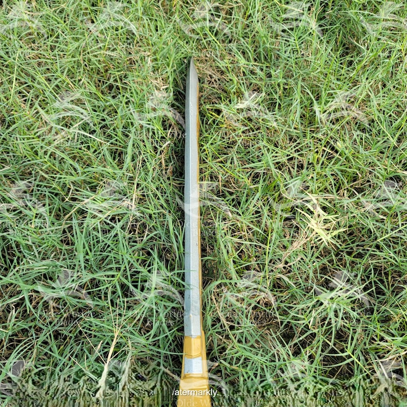 May include: A silver and gold sword lying on a bed of green grass.