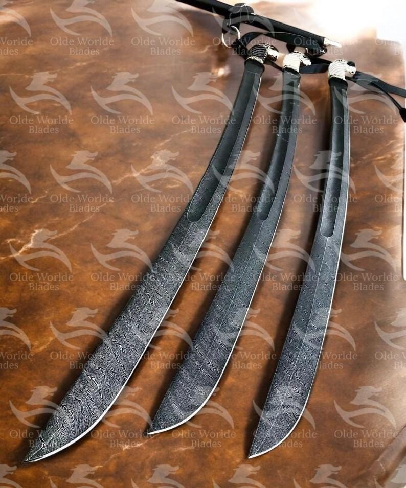 May include: Three black swords with intricate patterns on the blades. The swords are arranged in a fan shape on a brown wooden surface.