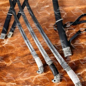 May include: Three decorative swords with intricate metalwork and ornate handles. The swords have black leather sheaths and are displayed on a brown marble surface.