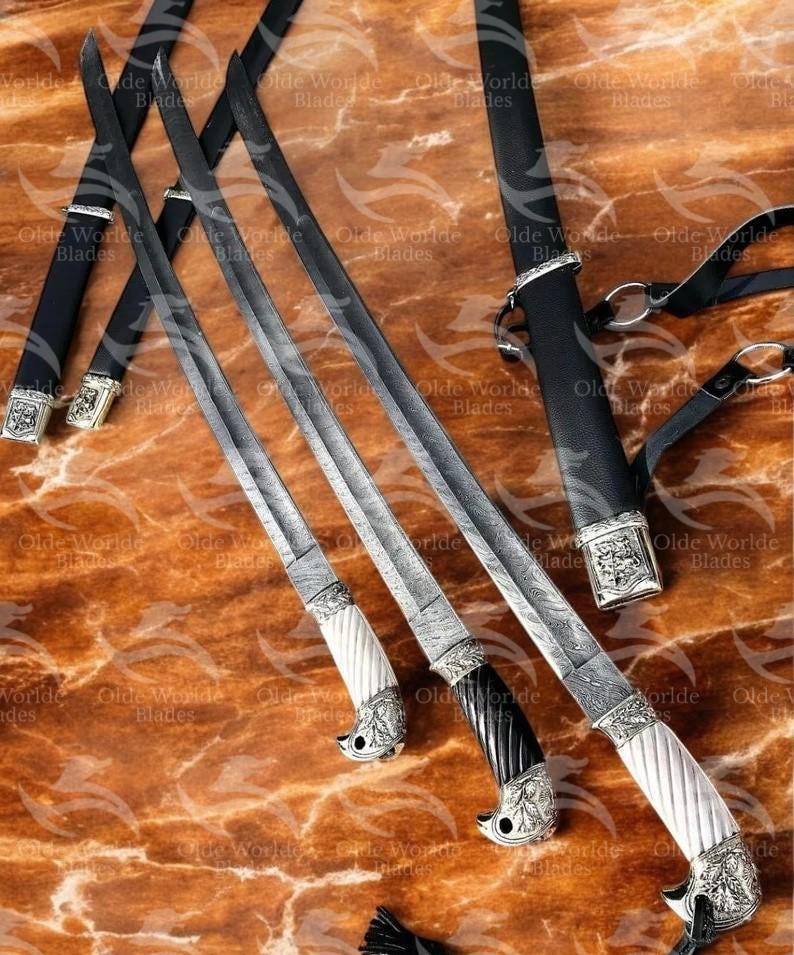 May include: Three decorative swords with intricate metalwork and ornate handles. The swords have black leather sheaths and are displayed on a brown marble surface.