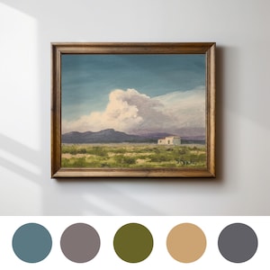 May include: A framed landscape painting depicts a desert scene with a white building, mountains, and a large cloud under a blue sky. The artwork is in a wooden frame. The painting is signed in the lower right corner.