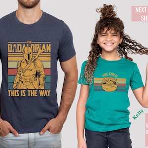 May include: Two t-shirts, one navy blue and one teal. The navy shirt features a graphic of a Mandalorian character with the text "THE DADALORIAN THIS IS THE WAY." The teal shirt displays "THE CHILD" with a graphic of a character in a pod.