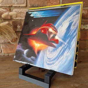 May include: A black vinyl record stand with a record on top. The record cover features a red spaceship flying through a blue and white cloudy sky. The album title is "Afterburner" and the band name is "Iron Maiden".