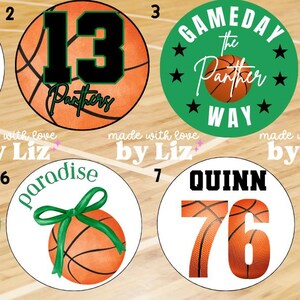 Puede incluir: Ocho diseños circulares con temas de baloncesto. Los diseños incluyen balones de baloncesto, lazos y texto como "Paradise Panthers" y "Gameday". Los colores incluyen naranja, verde, negro y blanco, con medidas en cm.