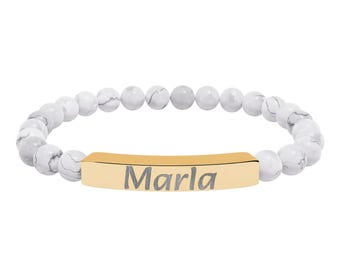 May include: A beaded bracelet with white and gray marble-like beads. The bracelet features a gold-colored bar with the name "Marla" engraved in gray letters. The bracelet is designed to be worn around the wrist.