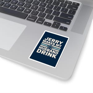 May include: A rectangular sticker with the text "JERRY MAKES MY HUSBAND DRINK" in white, with a star and stripes design, on a navy blue background. The sticker is placed on a silver laptop.