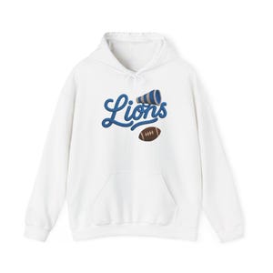 May include: A white hooded sweatshirt featuring a blue embroidered script that reads Lions. Above the text is a blue and white megaphone, and below the text is a brown football with white laces. The garment includes a front kangaroo pocket.