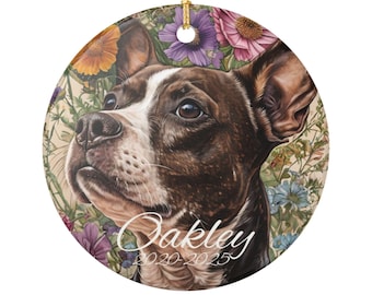 May include: Round ceramic ornament featuring a dog portrait with a floral background. The dog is brown and white, with a focused expression. The name "Oakley" and the years "2020-2025" are written on the ornament.