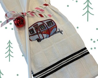 Puede incluir: Paño de cocina blanco con borde a rayas negras y diseño de caravana bordada. Una cuchara de madera blanca está atada a la toalla con una cinta a rayas y un adorno rojo. La toalla tiene un patrón texturizado a cuadros.