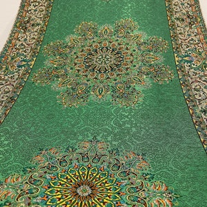 May include: A green table runner with a paisley design. The runner has a border with a floral pattern. The runner is made of a soft, textured fabric.