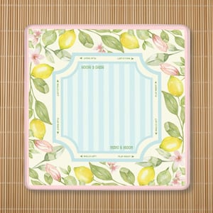 K&ouml;nnte beinhalten: Quadratische Mahjong-Matte mit hellrosa Rand, mit einem Aquarelldesign aus Zitronen, Bl&auml;ttern und rosa Bl&uuml;ten. Die Mitte hat ein hellblaues Streifenmuster mit den Worten "MAHI & MOON".