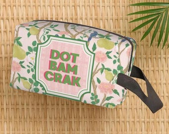May include: A rectangular cosmetic bag with a floral pattern of pears and pink flowers on a light pink background. The bag has a black handle and the text "DOT BAM CRAK" in a pink and green frame.