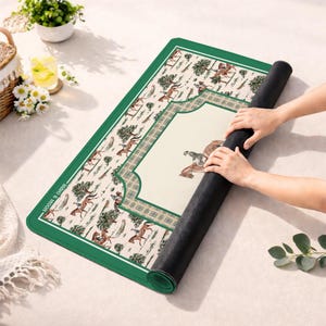 Puede incluir: Una alfombrilla rectangular con borde verde oscuro y centro color crema que presenta un patr&oacute;n ecuestre repetitivo de caballos y jinetes entre &aacute;rboles. La alfombrilla tiene un marco a cuadros y el texto "man & moon" impreso en el lado izquierdo.