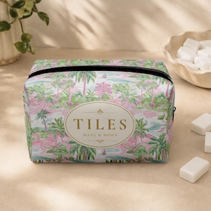 May include: A rectangular zippered pouch featuring a pink and green tropical palm tree pattern. Centered on the front is an oval gold-bordered label with the text TILES and MAHJ & MOON printed in gold lettering against a cream background.