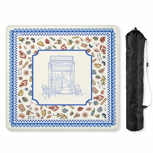 Puede incluir: Una manta de picnic cuadrada con fondo crema, borde de greca azul y una ilustraci&oacute;n central de una fachada de restaurante con la etiqueta RISTORANTE. El patr&oacute;n circundante incluye iconos coloridos de comida y vida marina.