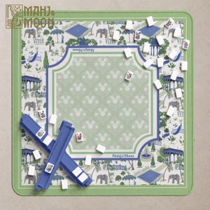 May include: A square green Mahj & Moon game mat featuring a repeating pattern of elephants, peacocks, and garden structures. The center has a light green floral motif bordered by blue lines. Two blue tile racks and white game tiles are included.