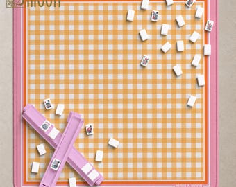 以下が含まれることがあります： 黄色と白のギンガムチェック柄の正方形のゲームマットで、オレンジとピンクのストライプで縁取られています。マットの隅と下部には「MAHJ & MOON」の文字が記されています。マットの上には、白い麻雀牌と2つのピンク色の牌ラックが散らばっています。