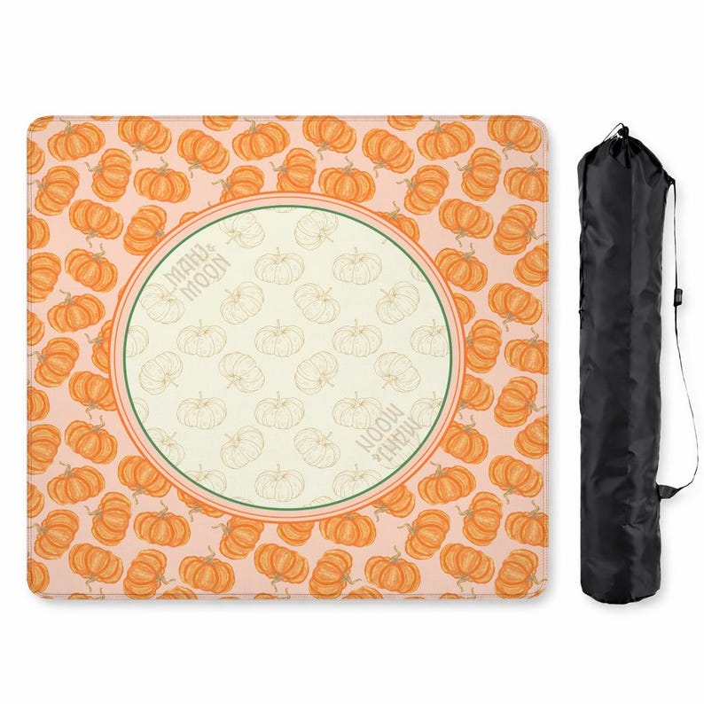 May include: A rectangular, pumpkin-themed picnic blanket with a repeating pattern of orange pumpkins on a light pink background. The center features a circular design with pumpkin outlines and the text "MAHU & MOON". A black carrying bag is included.