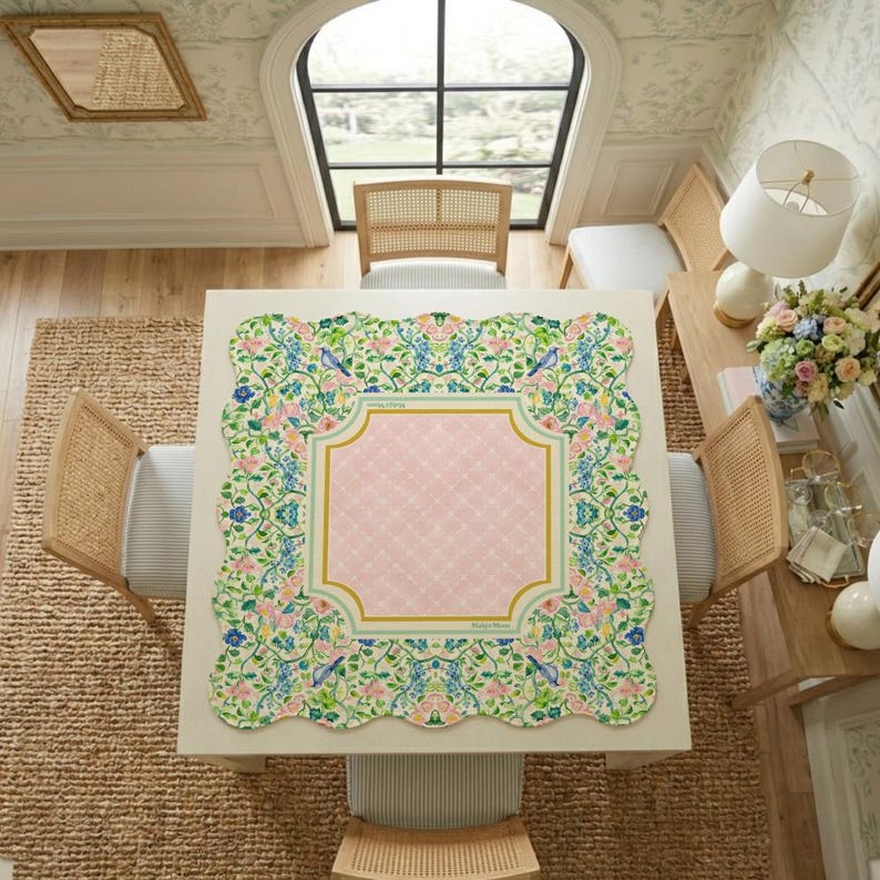 May include: A square tablecloth with a scalloped edge featuring a central light pink diamond-patterned panel framed by a gold border. The border is surrounded by a vibrant floral and bird print in shades of green, blue, pink, and yellow.