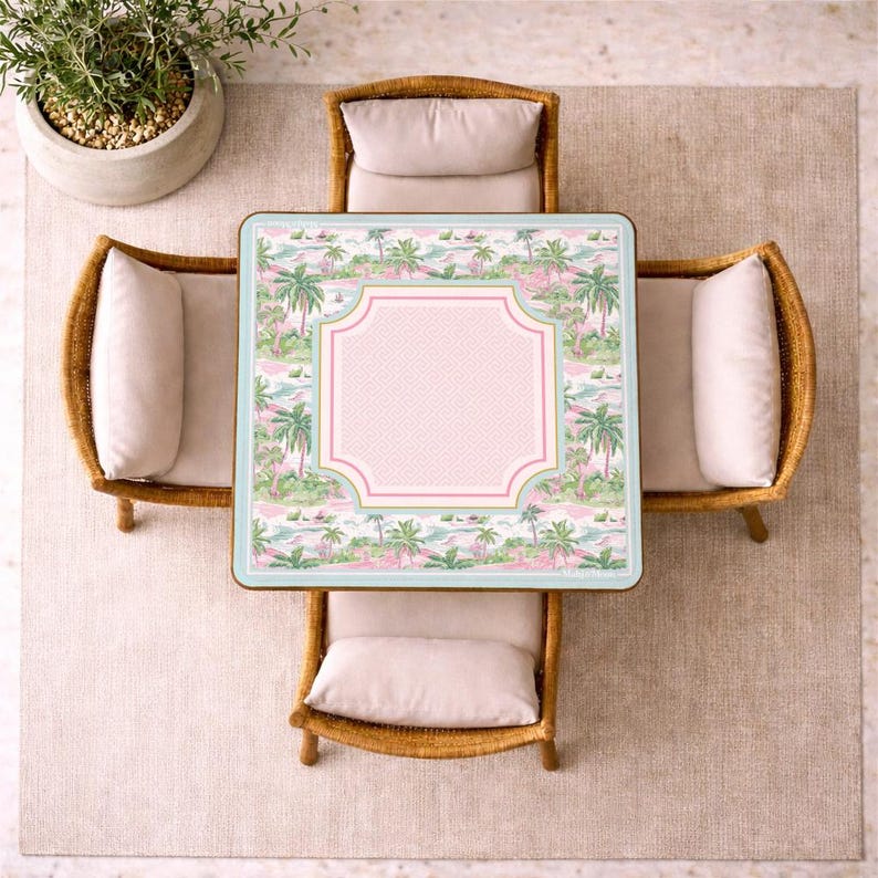 May include: A square table with a light blue border and a tropical pattern featuring palm trees and pink accents. The center has a pink geometric frame. Four rattan chairs with light beige cushions are arranged around the table.