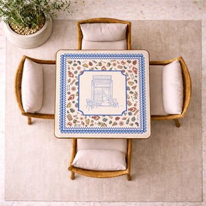 Puede incluir: Una mesa de comedor cuadrada con superficie blanca, borde azul y una ilustraci&oacute;n central de la fachada de un restaurante con la palabra RISTORANTE, rodeada de peque&ntilde;os iconos coloridos de comida y bebida, junto a cuatro sillas de mimbre.