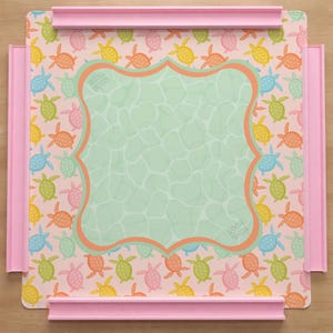 May include: A square puzzle board with a light pink background featuring a repeating pattern of small colorful turtles in yellow, orange, green, and blue. A central light green scalloped frame has a water-like texture and the text Mahi Moon.