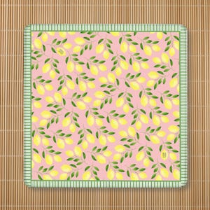 May include: A square fabric napkin featuring a repeating pattern of yellow lemons and green leaves on a light pink background, framed by a green and white striped border. The fabric has a small rectangular tag with text on the surface.