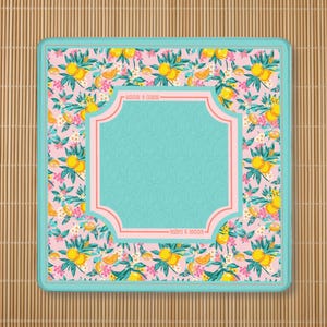 May include: A square coaster featuring a pink background with a repeating pattern of yellow lemons, green leaves, and small white flowers. A central teal scalloped frame with a light pink border contains the text "MAHJ & MOON" at the top and bottom.