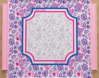 May include: A pink serving tray with a paisley design in white, pink, and blue. The tray has a rectangular center with a white paisley pattern framed by a pink and blue border. The words "MAHI & MOON" are printed on the tray.