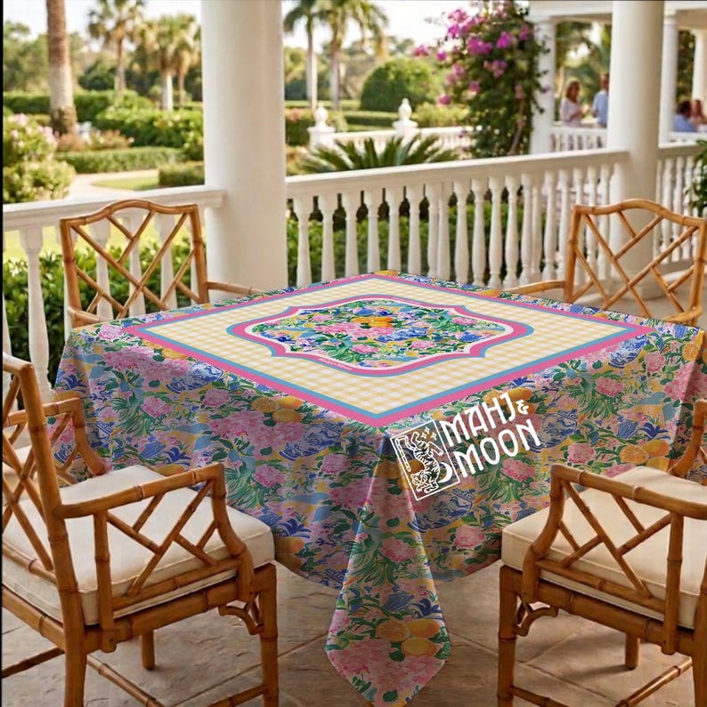 May include: A square tablecloth featuring a vibrant floral and citrus pattern with pink, yellow, and green tones, centered by a yellow and white gingham square with a pink border. The fabric displays the text MAHJ & MOON in white lettering.
