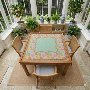 May include: A square table mat featuring a repeating pattern of small, colorful sea turtles in shades of pink, yellow, orange, and green. The center of the mat displays a large, light green scalloped frame with a subtle, textured pattern.