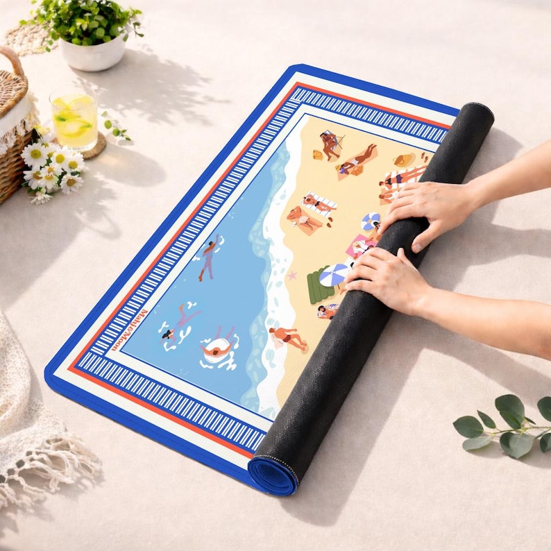 May include: A rectangular beach-themed mat with a blue border and a detailed illustration of a beach scene. The mat features people sunbathing, swimming, and relaxing on the sand. The mat is being rolled up, revealing its black underside.