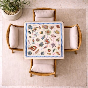 May include: A square table with a white surface featuring a blue wave border and colorful illustrations of seafood, fruit, wine, and bread. The table is surrounded by four light-colored wicker chairs with beige cushions, viewed from directly above.