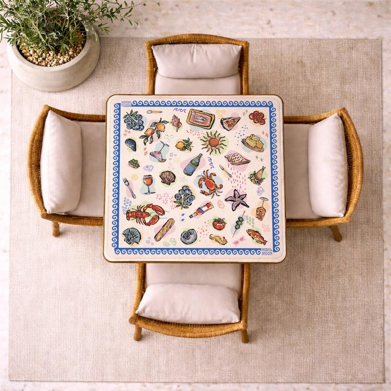 May include: A square table with a white surface featuring a blue wave border and colorful illustrations of seafood, fruit, wine, and bread. The table is surrounded by four light-colored wicker chairs with beige cushions, viewed from directly above.