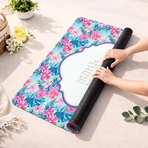 May include: A rolled yoga mat with a colourful floral pattern in pink, blue, and green. The mat has a white central section with the text "MAHJ & M". A person is rolling up the mat.