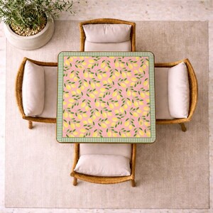 May include: A square table featuring a pink surface with a repeating pattern of yellow lemons and green leaves, surrounded by four chairs with light beige cushions and woven frames, viewed from directly above in a top-down perspective.