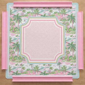 Op de afbeelding: Een vierkant decoratief dienblad met een tropisch eilandontwerp. De lade heeft een roze frame en accenten, een lichtblauwe rand en een centraal roze paneel met een geometrisch patroon. Het tropische ontwerp omvat palmbomen en een strandsc&egrave;ne.