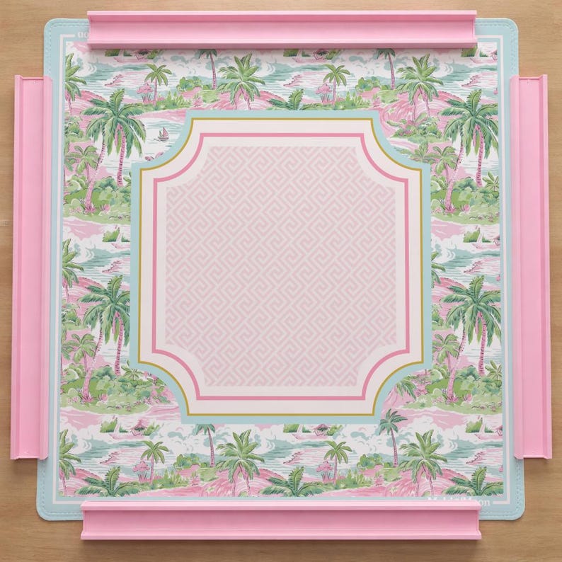 Op de afbeelding: Een vierkant decoratief dienblad met een tropisch eilandontwerp. De lade heeft een roze frame en accenten, een lichtblauwe rand en een centraal roze paneel met een geometrisch patroon. Het tropische ontwerp omvat palmbomen en een strandsc&egrave;ne.