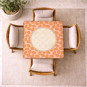 May include: Overhead view of a square table with a pumpkin pattern, surrounded by four wicker chairs with cream-colored cushions. The table has a central circular design with the words "Happy Moon". A potted plant sits nearby.