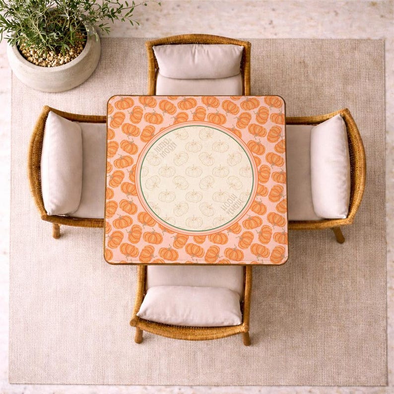 May include: Overhead view of a square table with a pumpkin pattern, surrounded by four wicker chairs with cream-colored cushions. The table has a central circular design with the words "Happy Moon". A potted plant sits nearby.